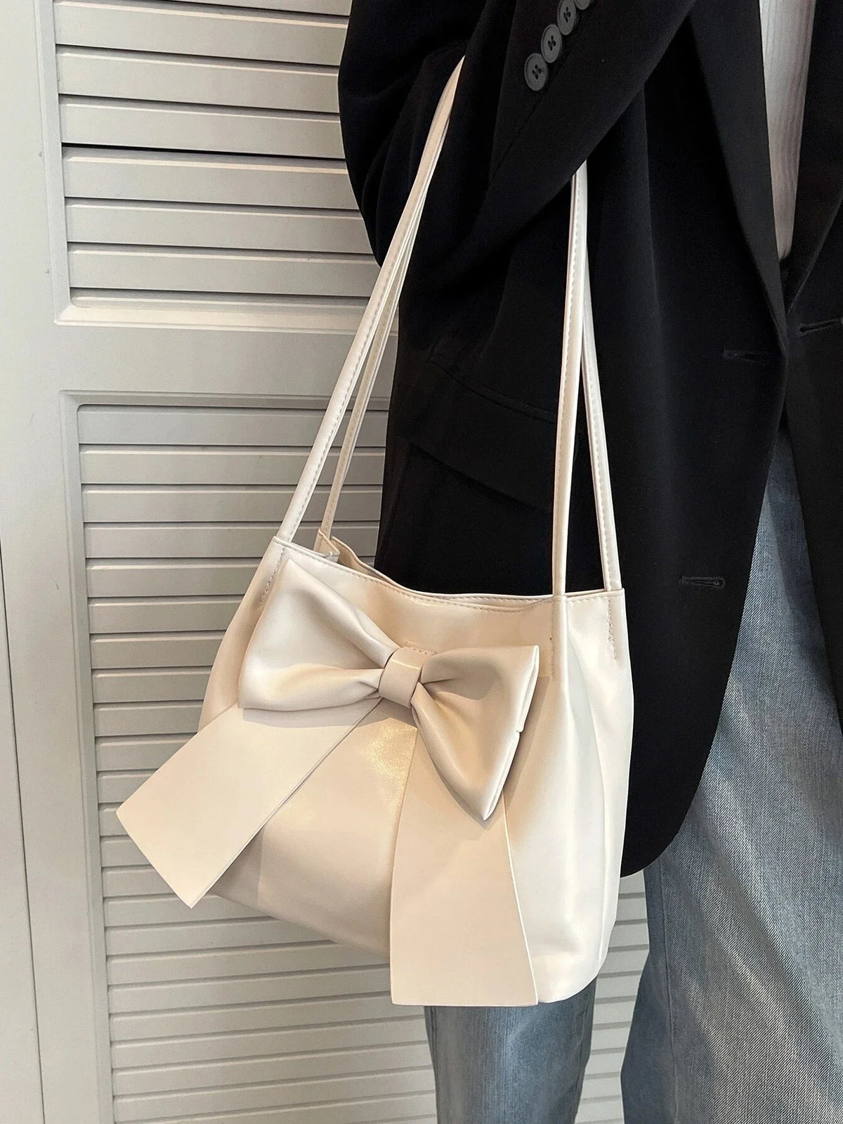 Blazer noir et jean clair, le sac écru à nœud pend le long du buste, bandoulière fine