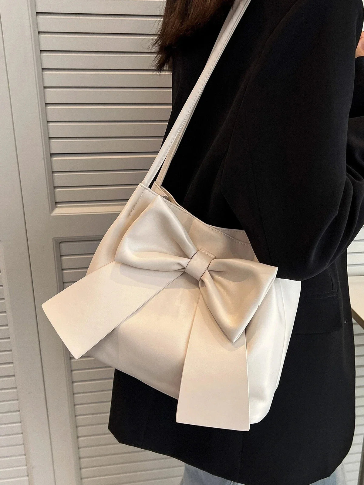 Épaule d'un blazer noir portant le sac écru, dont le grand nœud retombe sur le côté
