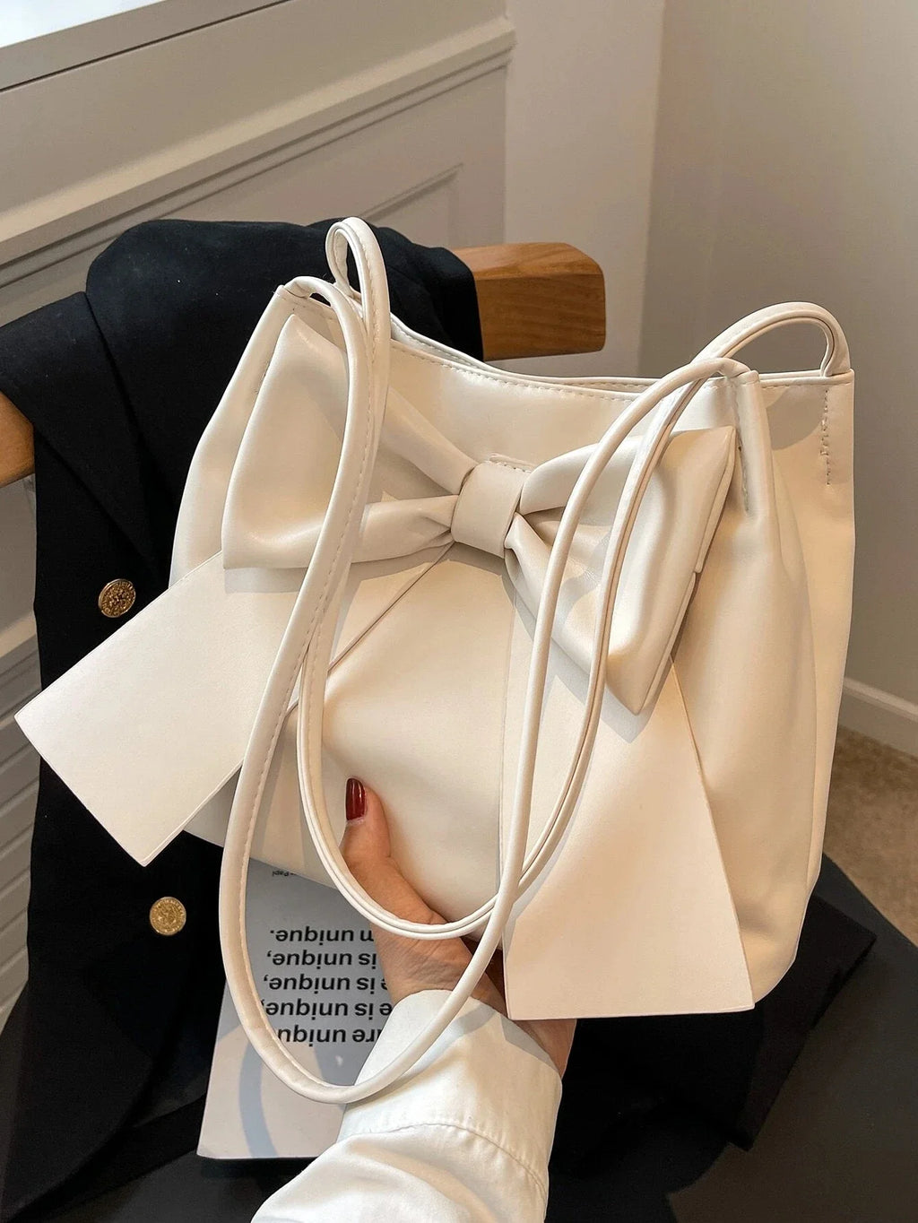 Main tenant le sac écru au-dessus d'un livre ouvert, nœud et plis souples bien visibles
