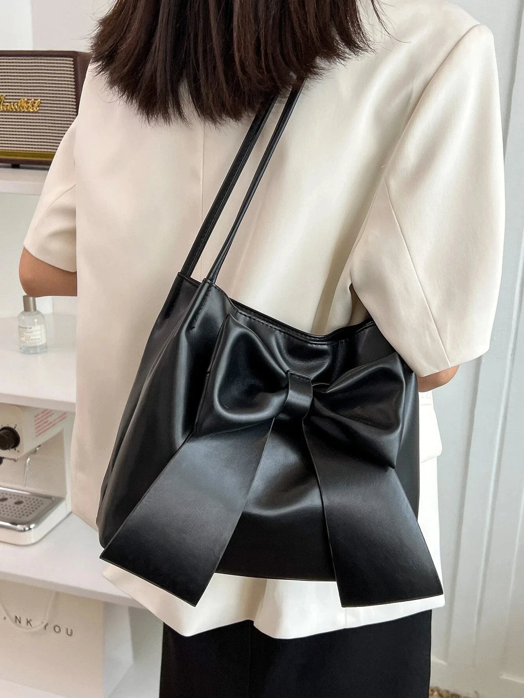 Bandoulière en travers du buste, le sac noir à nœud contraste avec une chemise blanche