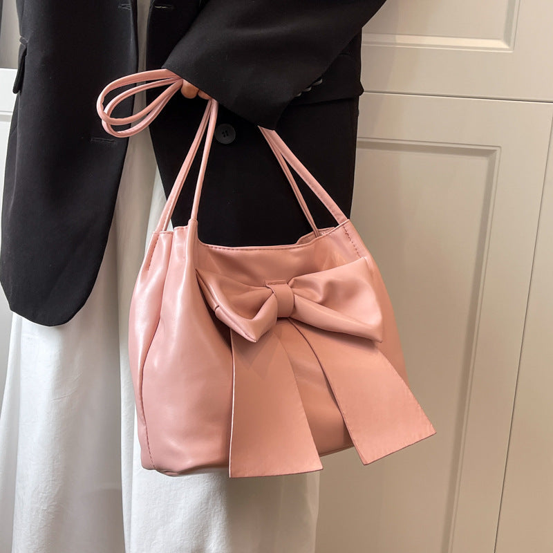 Deux anses courtes tenues au creux du bras pour ce sac rose plissé au nœud volumineux