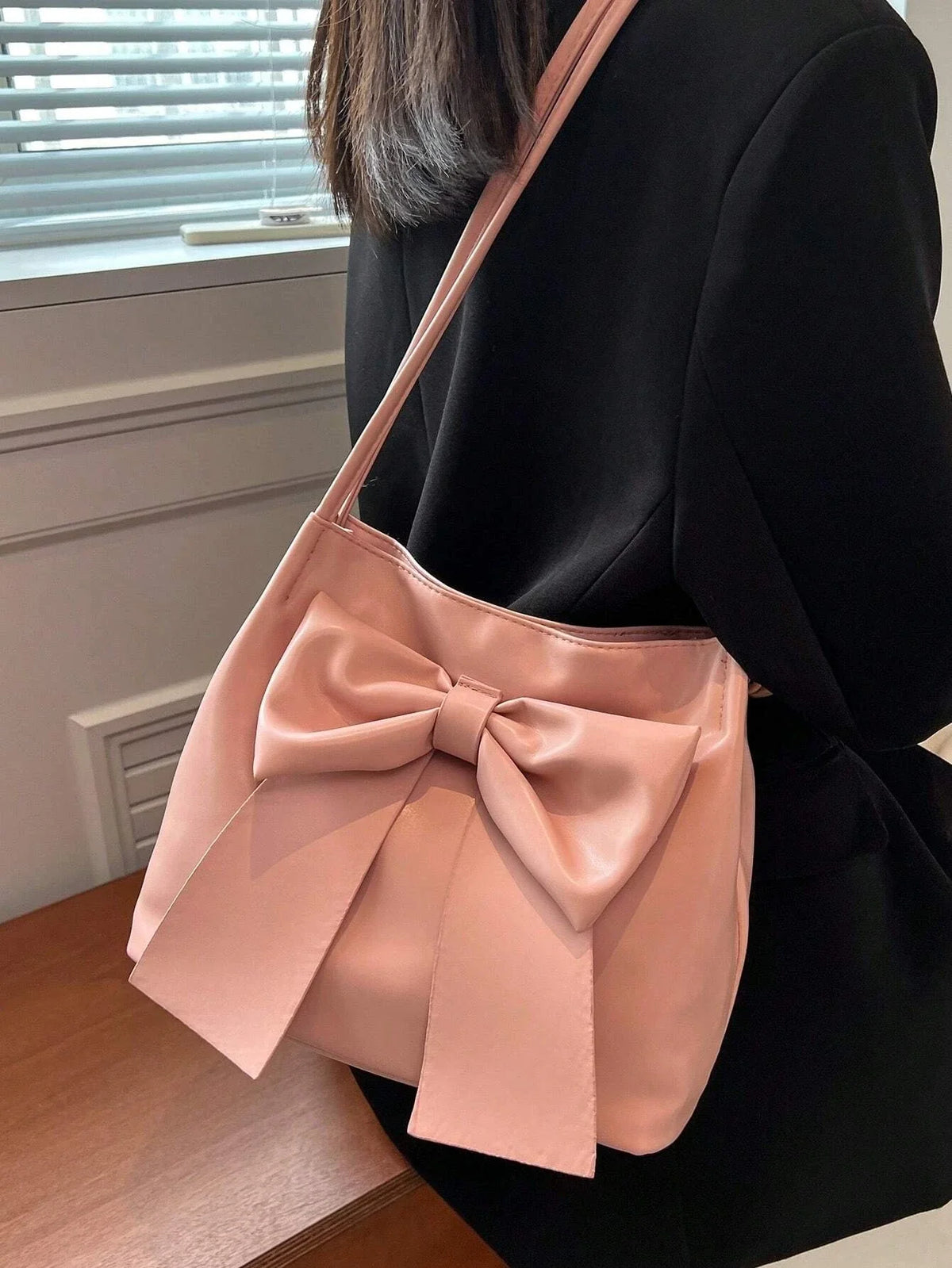 Sur l'épaule d'un blazer noir, le sac rose à gros nœud laisse voir ses plis nets et son anse