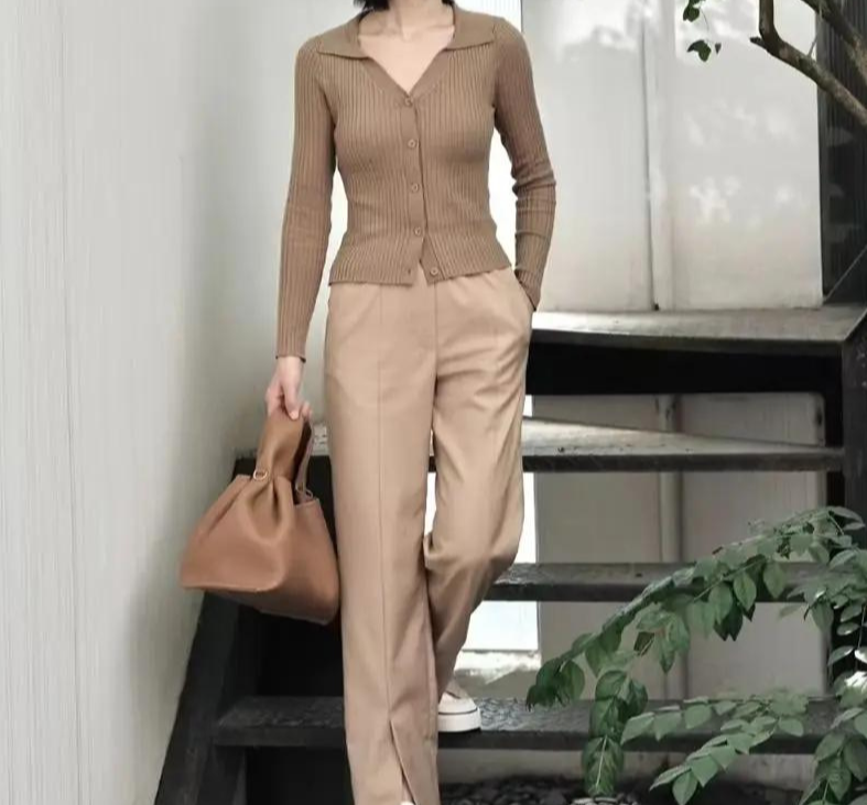 Silhouette complète en tenue beige descendant un escalier, le pochon camel au bout du bras