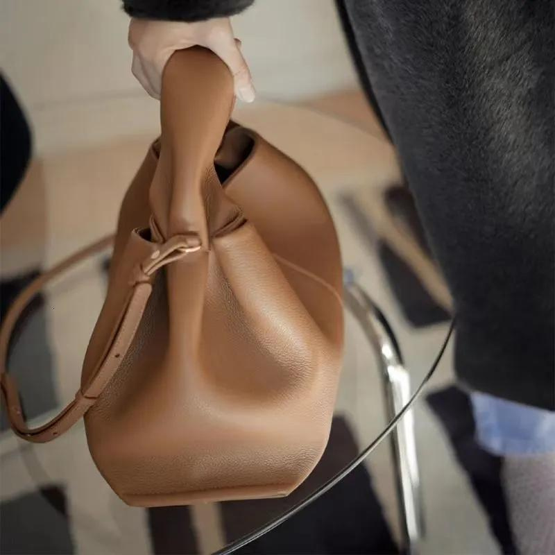 Main glissée sous l'anse du sac camel, corps souple qui se plisse au-dessus d'une table vitrée
