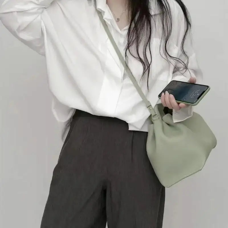 Bandoulière portée en croisé sur une chemise blanche, petit sac vert amande contre la hanche