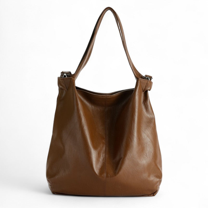 Marron caramel et cuir végan lisse, ce cabas seau affiche ses anses hautes et sa sangle réglable
