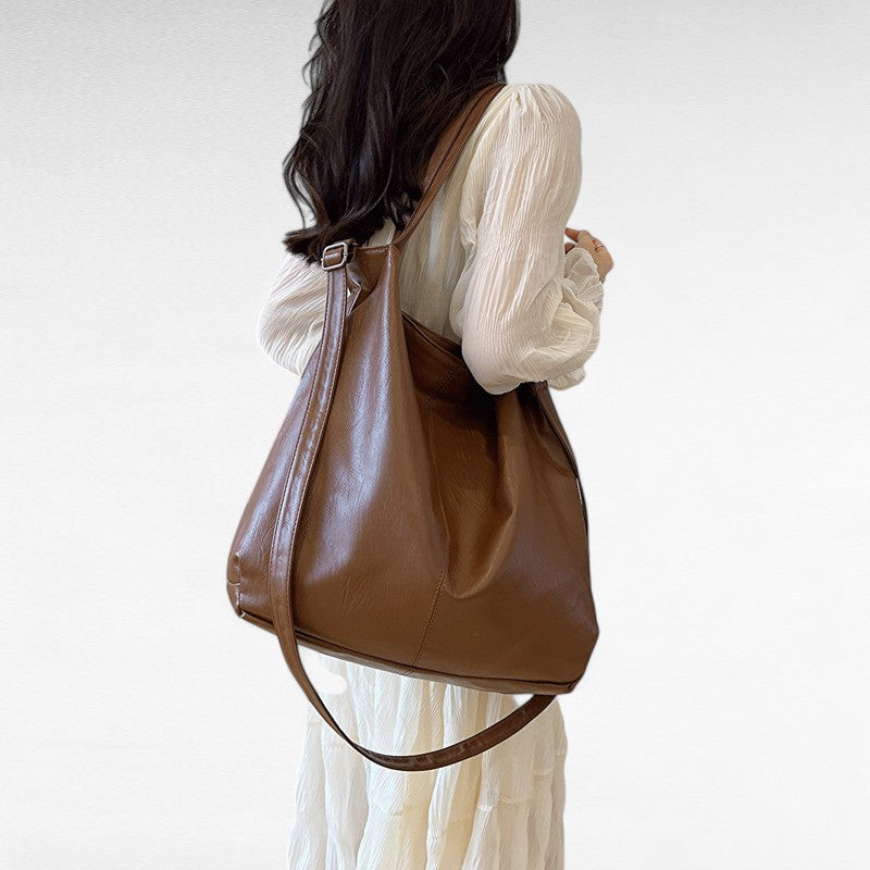 Robe blanche et fourre-tout marron cognac porté à l'épaule, bandoulière laissée pendante