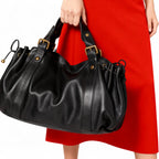 Tenu par ses deux anses devant une robe rouge, le sac noir déploie ses plis en éventail