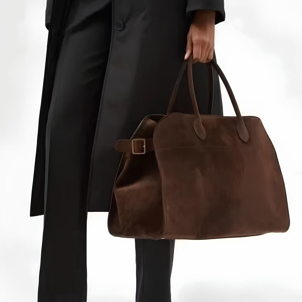Tenu à la main le long d'un manteau noir, le grand cabas marron chocolat garde sa tenue