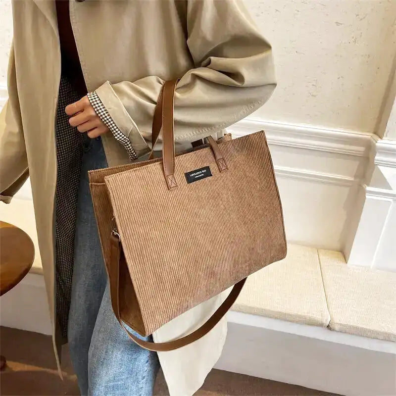 Glissé sous le bras sur un trench beige, le cabas camel côtelé garde une allure structurée