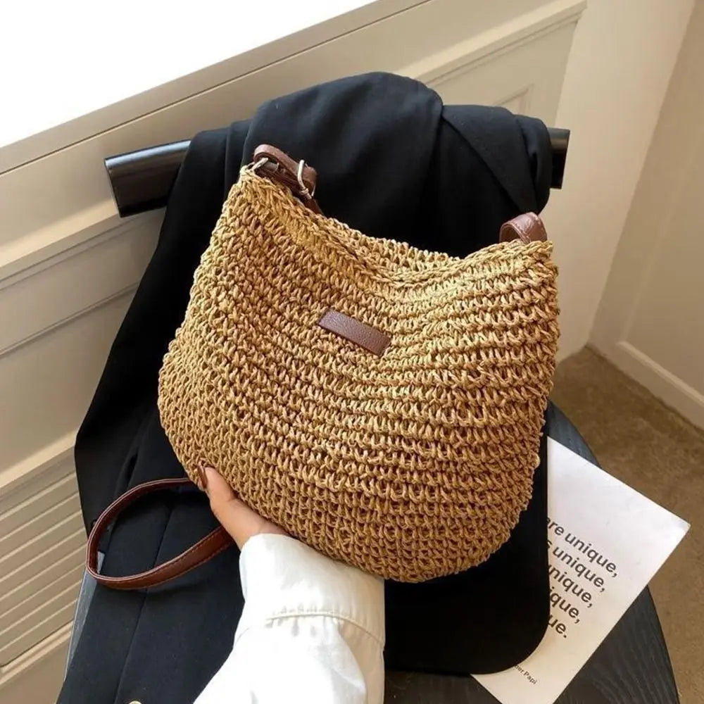 Tenu à la main devant un blazer noir, le sac en paille claire montre son maillage crocheté