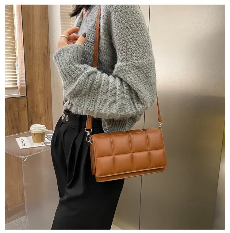 En bandoulière croisée sur un gilet gris, le petit sac cognac matelassé repose sur la hanche