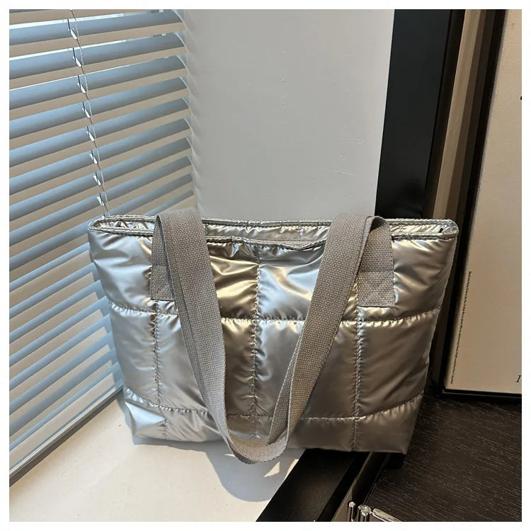 Devant un store vénitien, le sac argenté brillant capte la lumière, sangles retombant devant