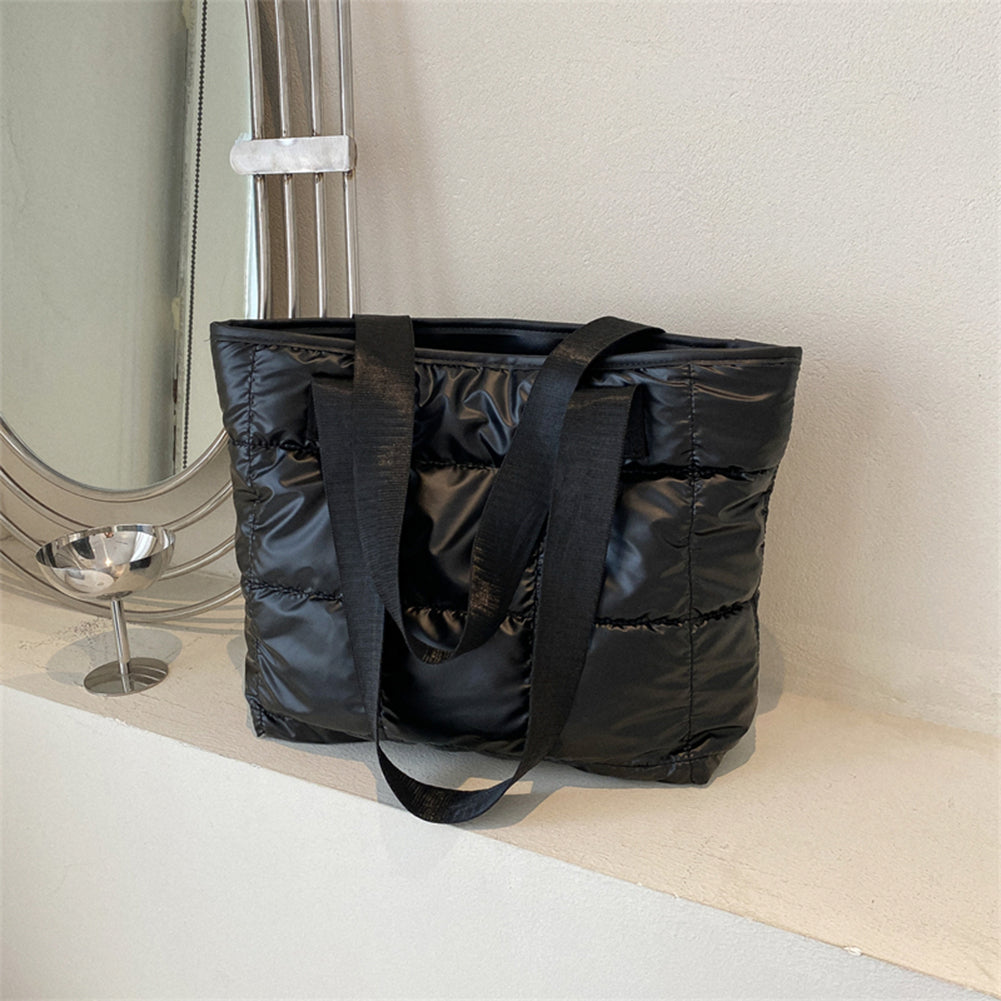 Nylon matelassé noir à surpiqûres carrées, le sac posé sur un rebord clair, anses tombantes