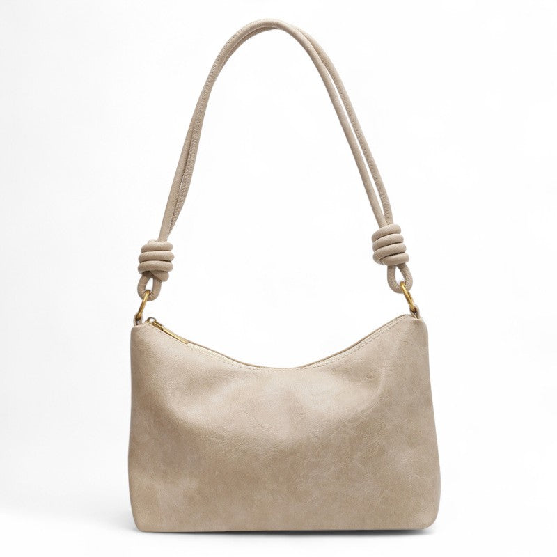 Écru sable et matière mate, le sac baguette est présenté de face avec son anse nouée aux extrémités