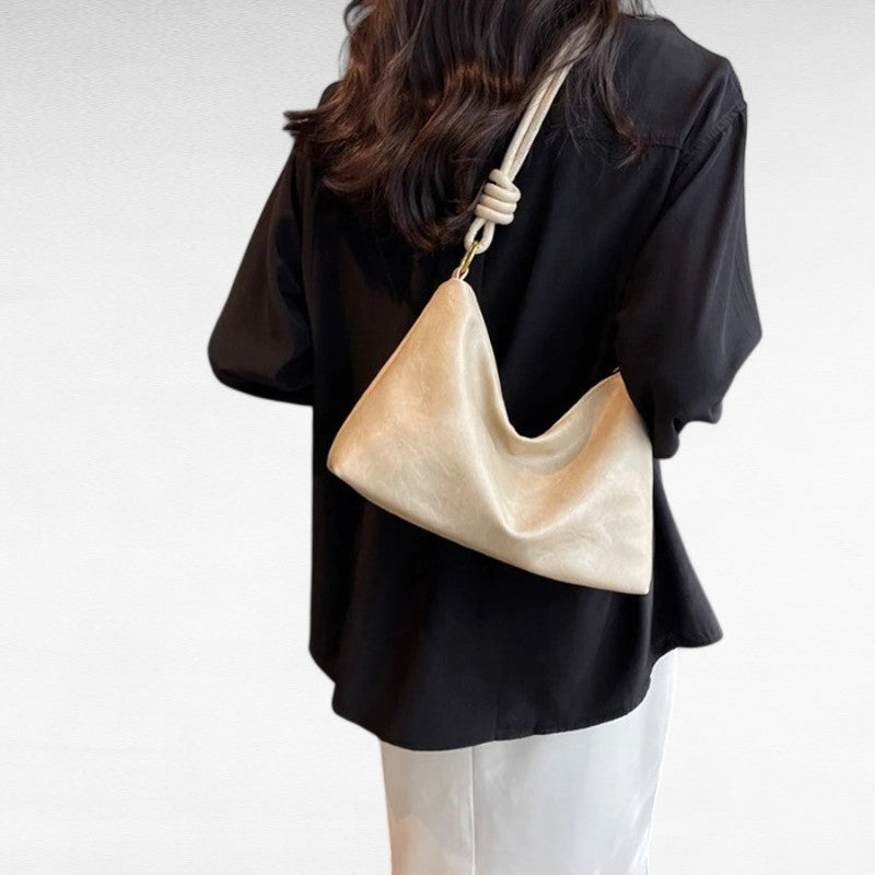Écru lumineux dans le dos d'une silhouette en chemise noire, le sac baguette se plisse au centre