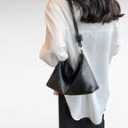 En pointe sous le bras d'une femme en chemise blanche, le sac baguette noir descend sur la hanche