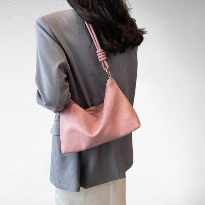 Rose poudré porté dans le dos sur un blazer gris, le sac baguette forme un pli souple en V