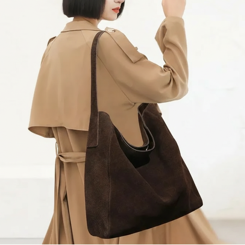 Sur un trench camel, le sac brun chocolat est porté à l'épaule, dos tourné vers l'objectif