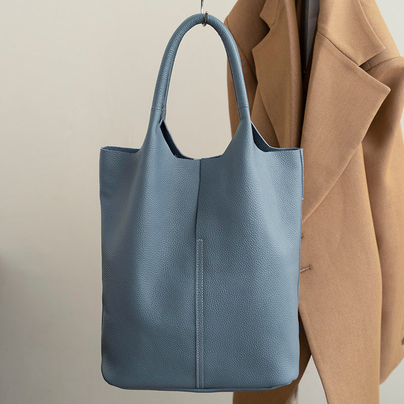 Suspendu près d'un manteau camel, le tote bleu gris montre son grain régulier et sa couture verticale
