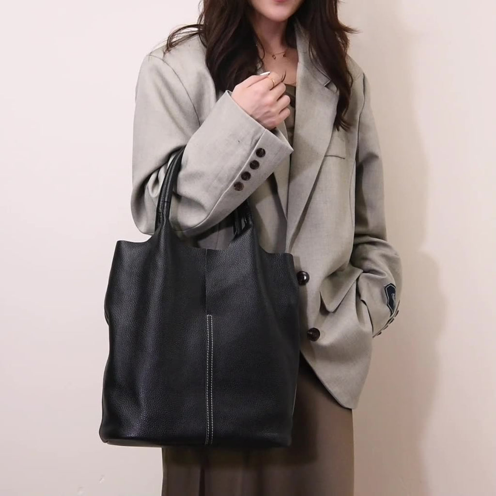 Porté au bras sur un blazer taupe, le sac noir grainé se plie légèrement sous son propre poids