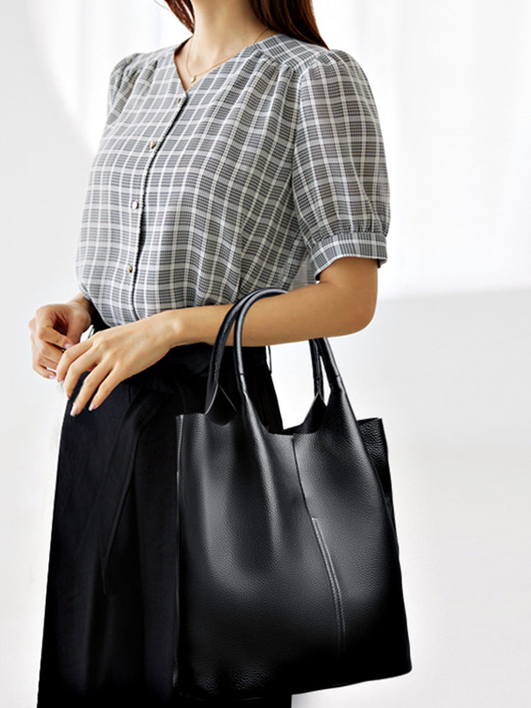 Au creux du bras devant une chemise à carreaux, le grand tote noir s'étire vers le bas du corps