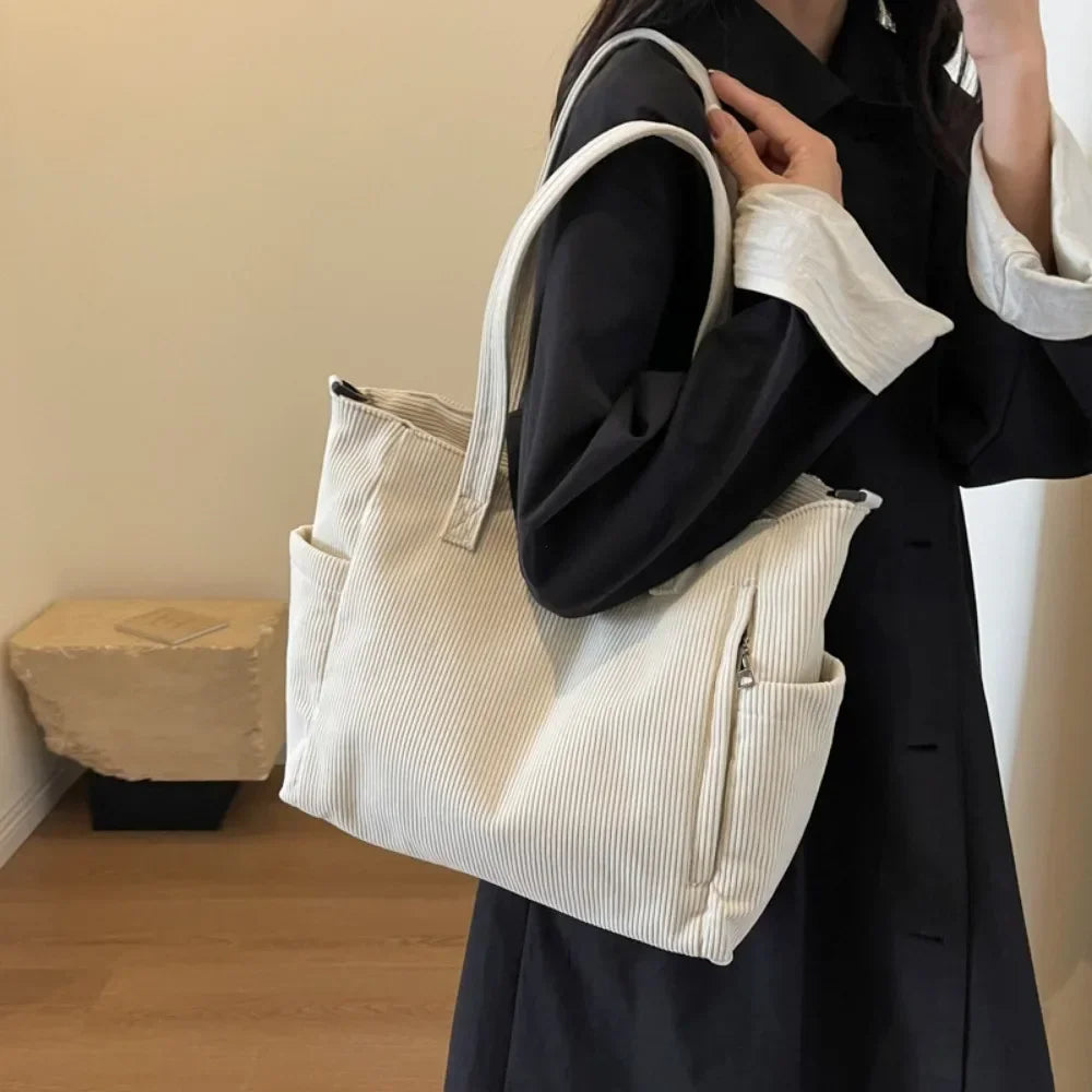 Au creux du bras sur un manteau noir, le grand sac écru en velours côtelé s'affaisse doucement