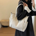 Au creux du bras sur un manteau noir, le grand sac écru en velours côtelé s'affaisse doucement