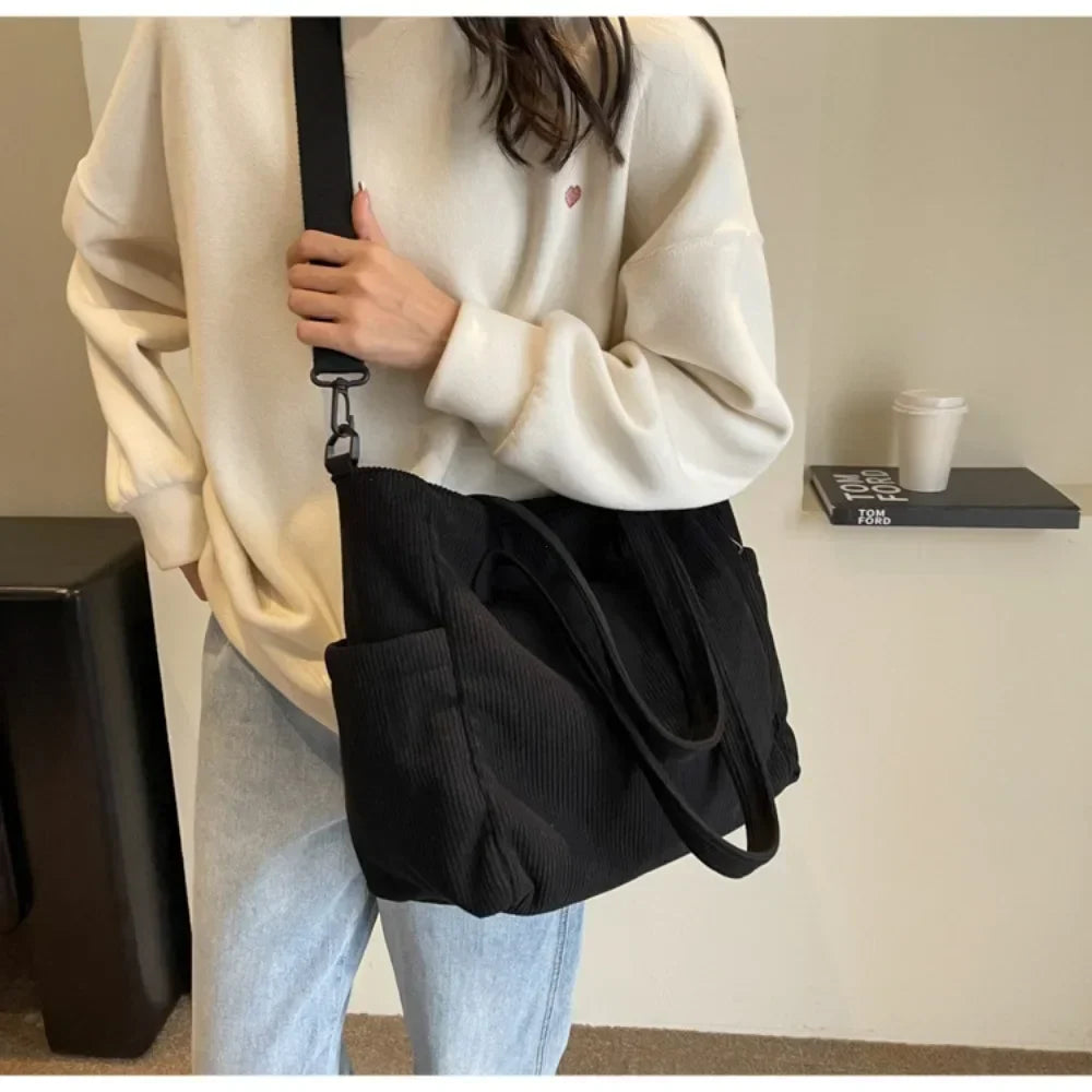 En croisé sur un sweat écru, le grand cabas noir descend sur la hanche, large sangle à l'épaule