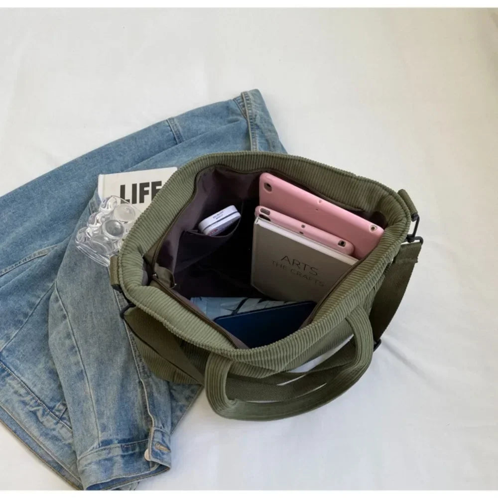 Ouvert sur un lit, le cabas vert laisse voir une tablette rose et une pochette dans son compartiment