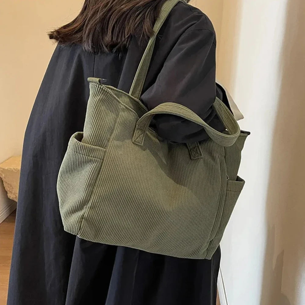 À l'épaule sur un manteau noir, le cabas vert olive côtelé garde ses anses courtes bien dressées