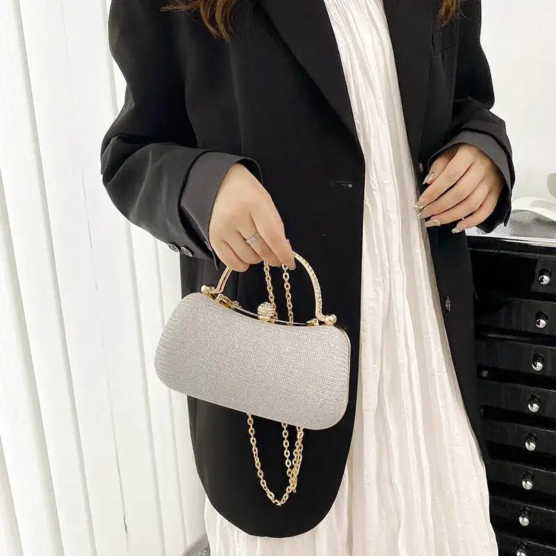 Tenue par son anse dorée devant un blazer noir, la minaudière argentée laisse pendre sa chaîne