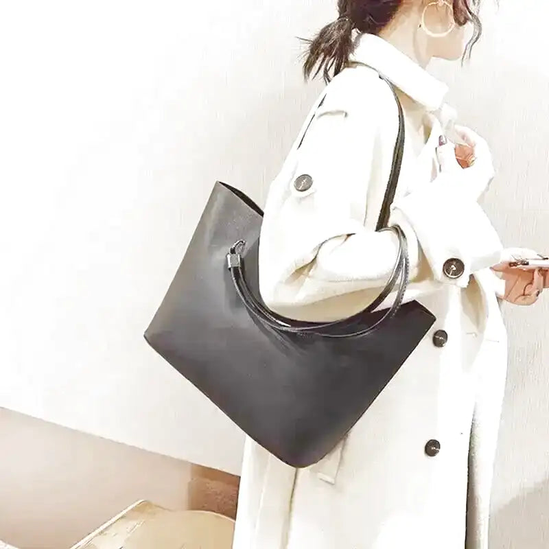 Manteau blanc et cabas noir tenu au creux du bras, anses rassemblées dans la main