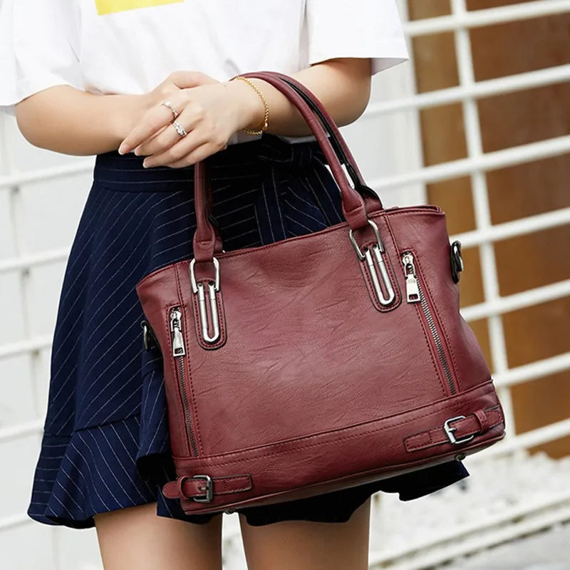 Mains posées sur les anses du sac bordeaux, tenu devant une jupe bleu marine rayée