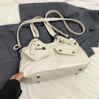 Version écru posée sur un drap gris, longue bandoulière enroulée et rivets argentés apparents