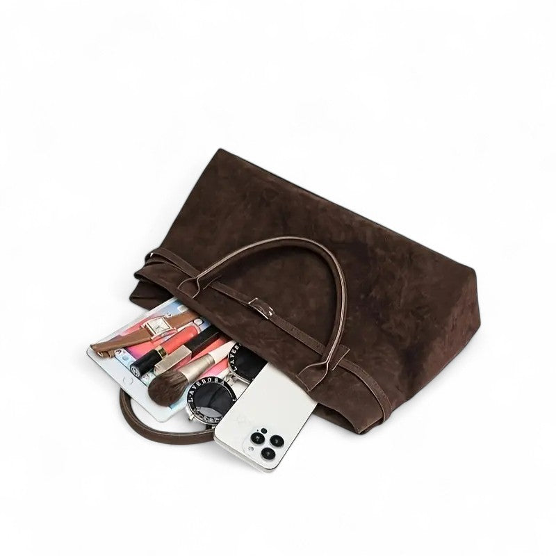 Contenu qui déborde du sac couché : carnet, rouges à lèvres, pinceau, montre et téléphone