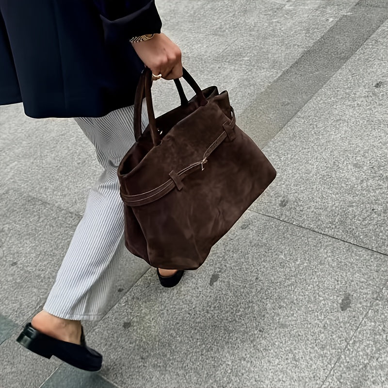 Tenu à la main dans la rue, le cabas brun café accompagne un pantalon rayé et une veste marine