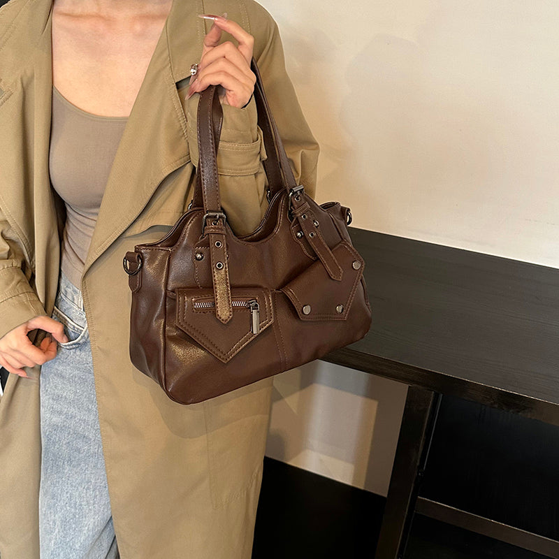 Suspendu au poignet devant un manteau kaki clair, le sac marron dévoile sa bandoulière détachable