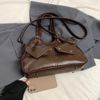 Étalé sur un drap gris, le sac brun chocolat voisine avec un téléphone posé à plat sur le lit