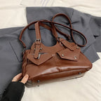Main soulevant le sac brun roux posé sur un drap gris, sangle et anses déployées tout autour