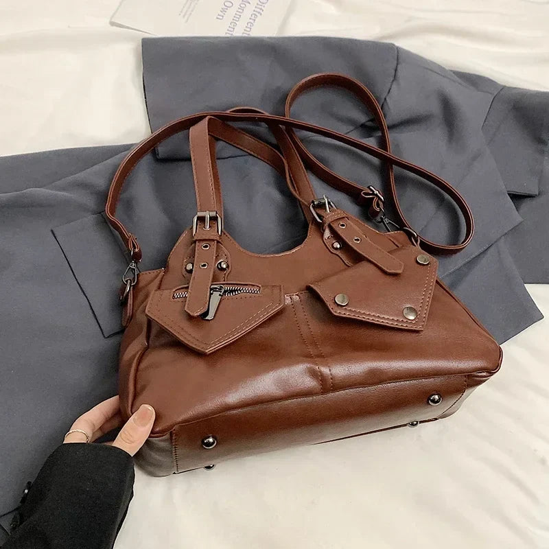 Main soulevant le sac brun roux posé sur un drap gris, sangle et anses déployées tout autour