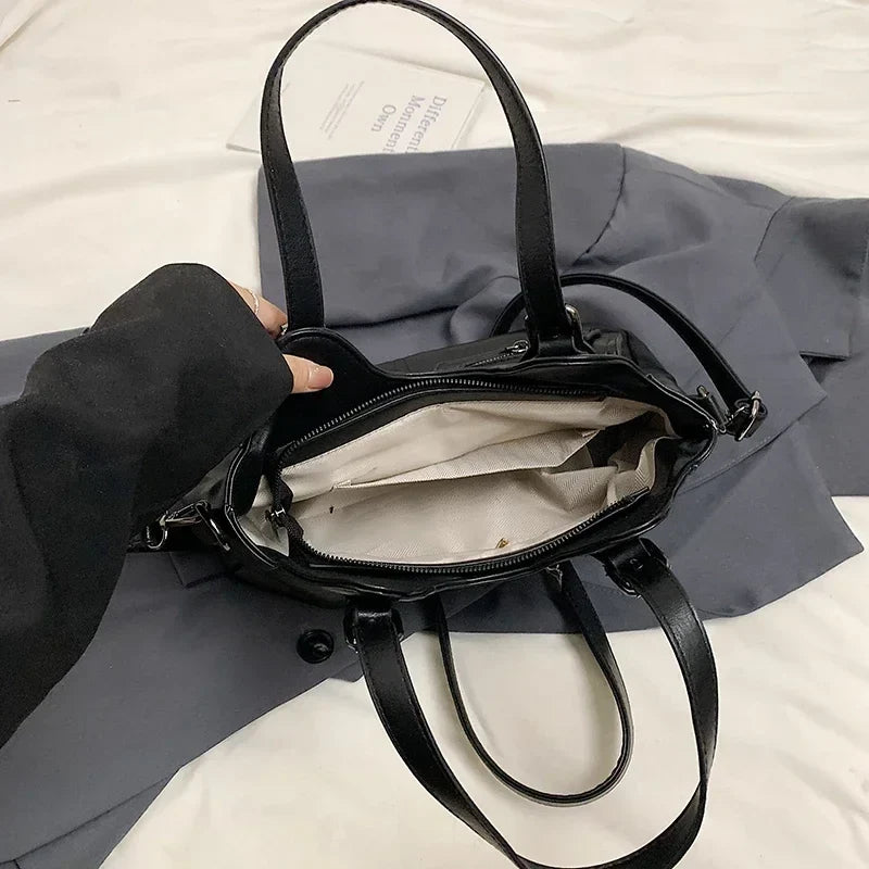 Ouvert par une main, l'intérieur clair du sac noir révèle sa poche plaquée et sa glissière centrale
