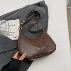 Hobo brun café posé de trois quarts sur une veste grise, sangle réglable tenue à la main