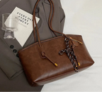 Posé sur une veste taupe, le cabas chocolat montre son flanc lustré et ses embouts dorés