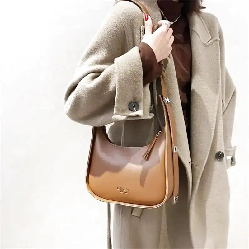 Bicolore brun et caramel, le sac remonte sous l'épaule d'un long manteau écru en laine