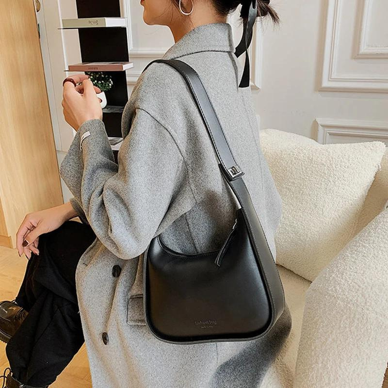 Accroché à l'épaule d'un manteau gris clair, le sac noir arrondi se découvre de dos, en salon