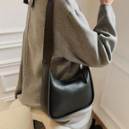 Épaule d'une veste grise portant la besace noire, volume compact posé contre la hanche