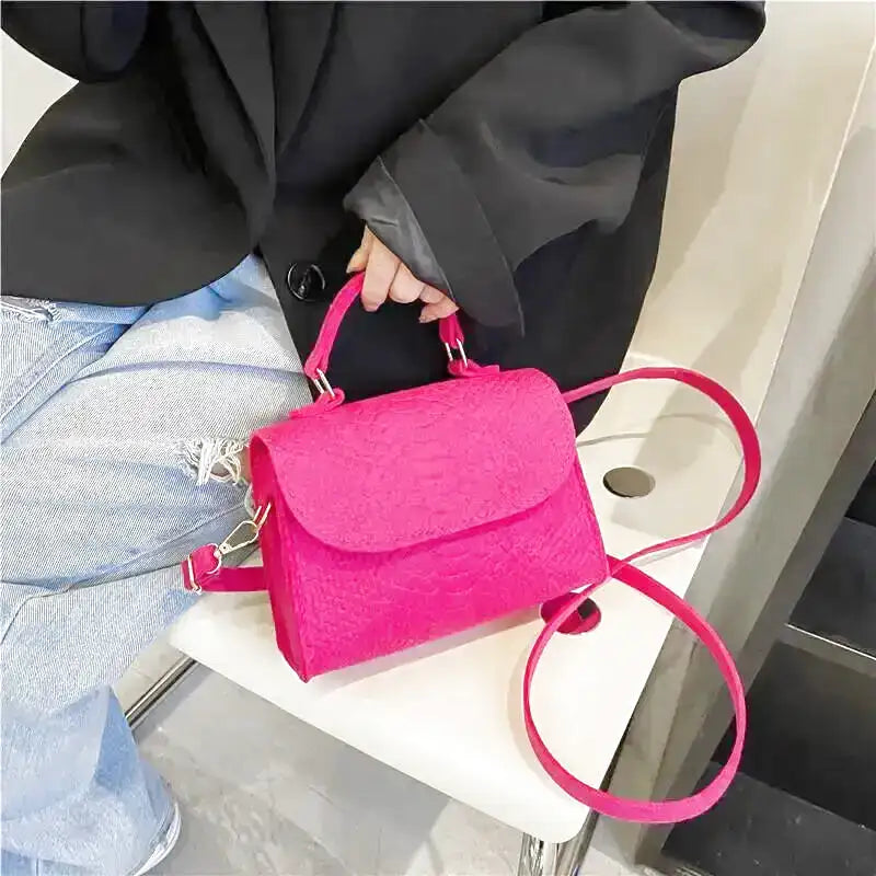 Le sac fuchsia posé sur une assise blanche déroule sa bandoulière à mousquetons argentés
