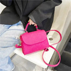 Le sac fuchsia posé sur une assise blanche déroule sa bandoulière à mousquetons argentés