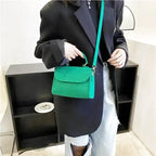 Porté en croisé sur une veste noire, le petit sac vert est tenu par son anse supérieure